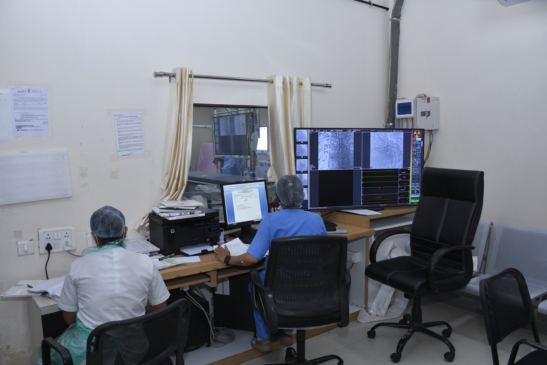 Cath Lab control room with clinical staff monitoring live angiography imaging on dual screens